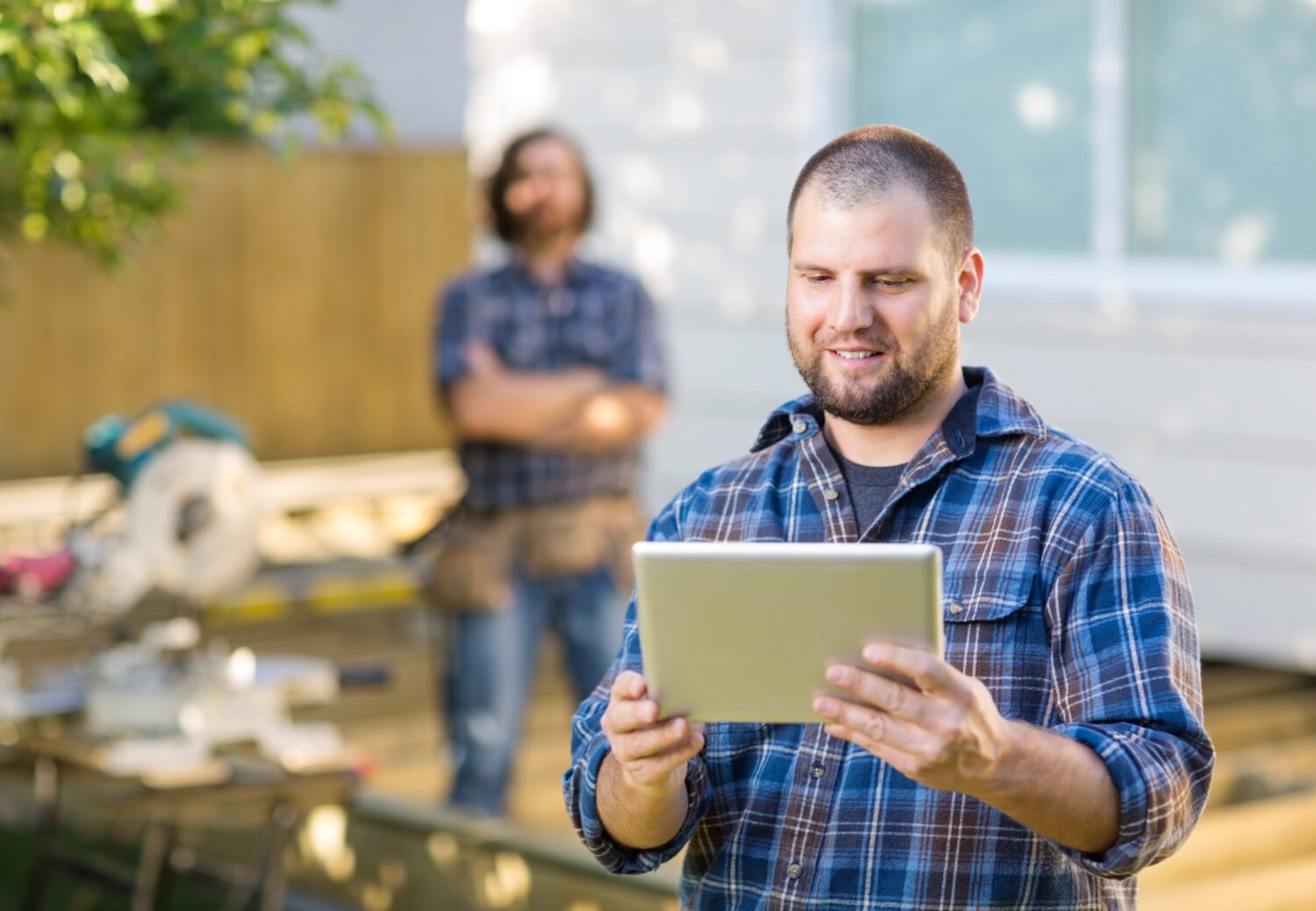 Carpenter Using Tablet With Coworker Standing In Background