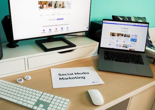 A desktop and laptop are on a table, and a sheet of paper has Social Media Marketing written on it.